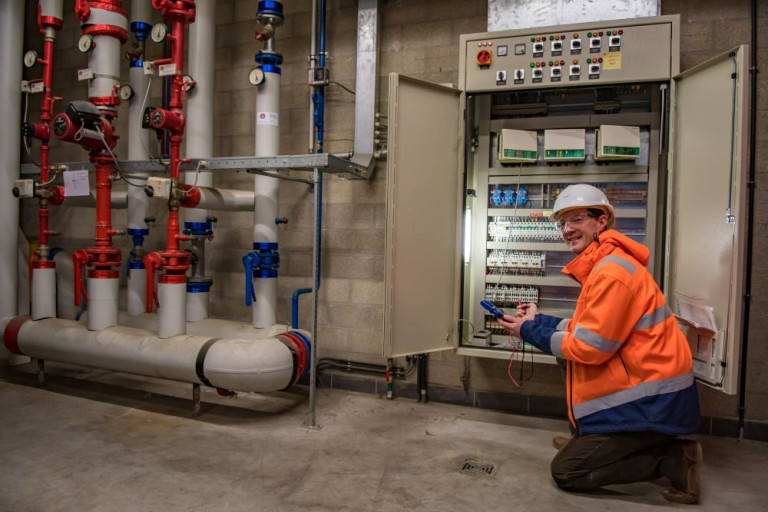 man met helm en fluorjas bedient elektriciteitskast
