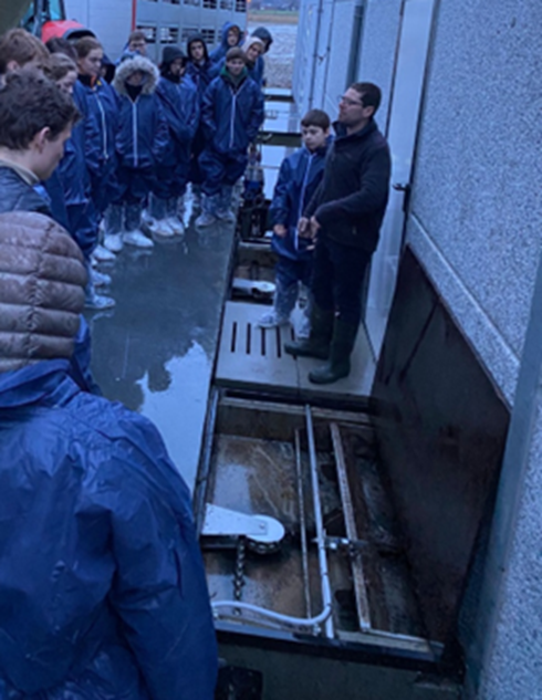 De mestschuif is tijdelijk in rust buiten de stal. Aangespannen door een tandwiel en aangedreven door motor met klein vermogen. De afdekplaten werden tijdelijk verwijderd om het systeem zichtbaar te maken.